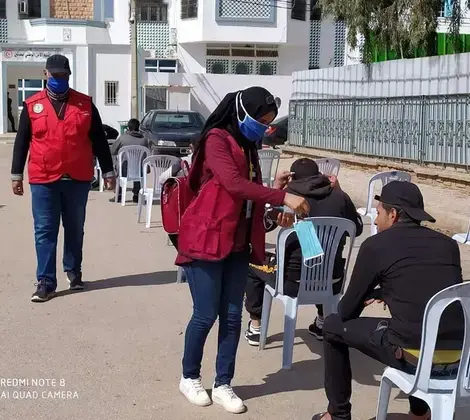 A Local Crisis Committee volunteer distributing protective masks to those waiting in line for essential services